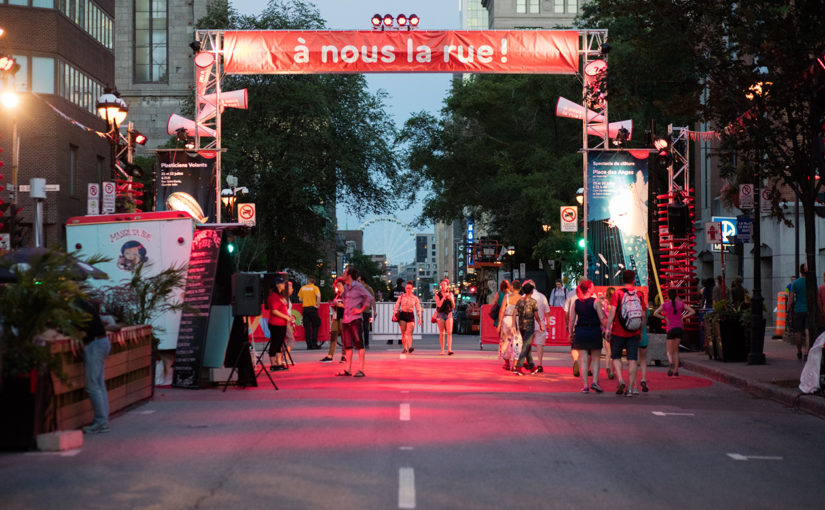 Passants attirés par l’arche rouge décoré de porte-voix à l’entrée du site d’événement sur la rue St-Denis le soir à Montréal