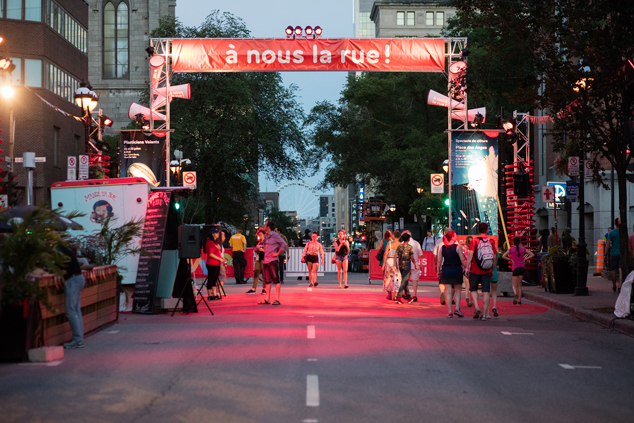 Passants attirés par l’arche rouge décoré de porte-voix à l’entrée du site d’événement sur la rue St-Denis le soir à Montréal