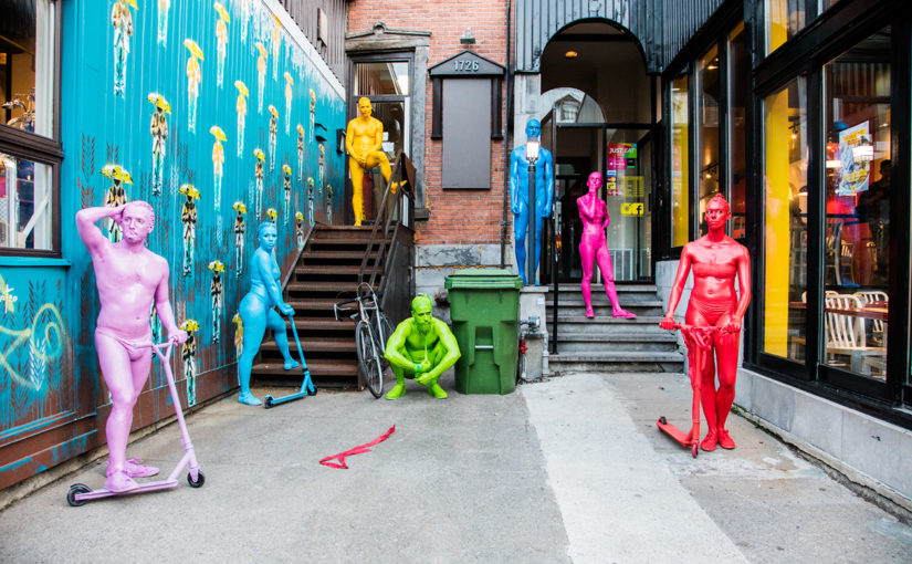 Personnages en trottinette colorés entourés d’art de rue dans une ruelle commerciale pour faire l’animation du parcours piéton