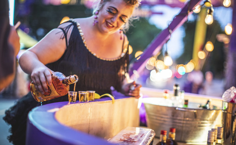 Gros plan d’une animatrice dans son costume versant de l’alcool derrière le bar mauve sur-mesure dans une ambiance festive