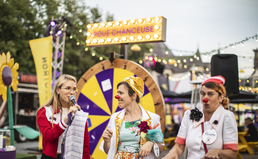 Personnages de cirque costumés devant la roue chanceuse qui tourne pour gagner un prix en plein coeur du décor forain illuminé