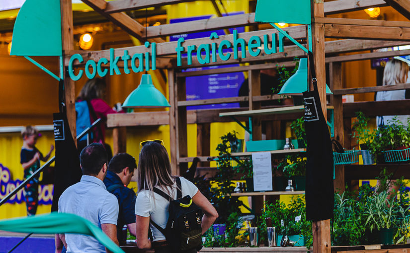 Participant faisant lui-même son drink au kiosque extérieur “Cocktail fraîcheur” fait de bois et décoré de lampes turquoises