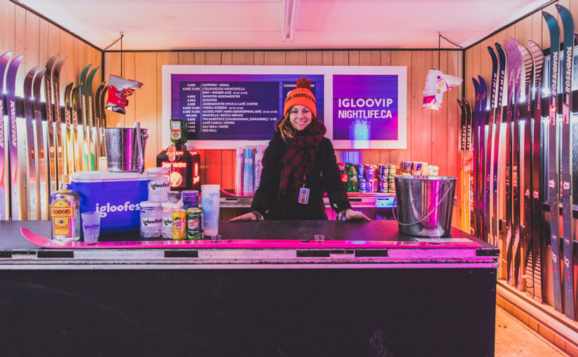 Barmaid derrière le bar à l’intérieur de la roulotte igloofest VIP décorée de vieux skis et de bottes suspendues à l’envers